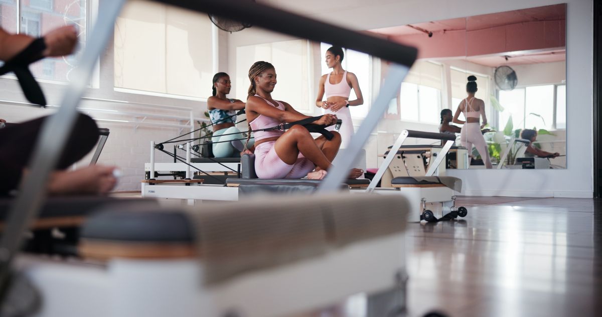 Group of women participating in a reformer Pilates class, exercising together on reformer machines in a bright studio