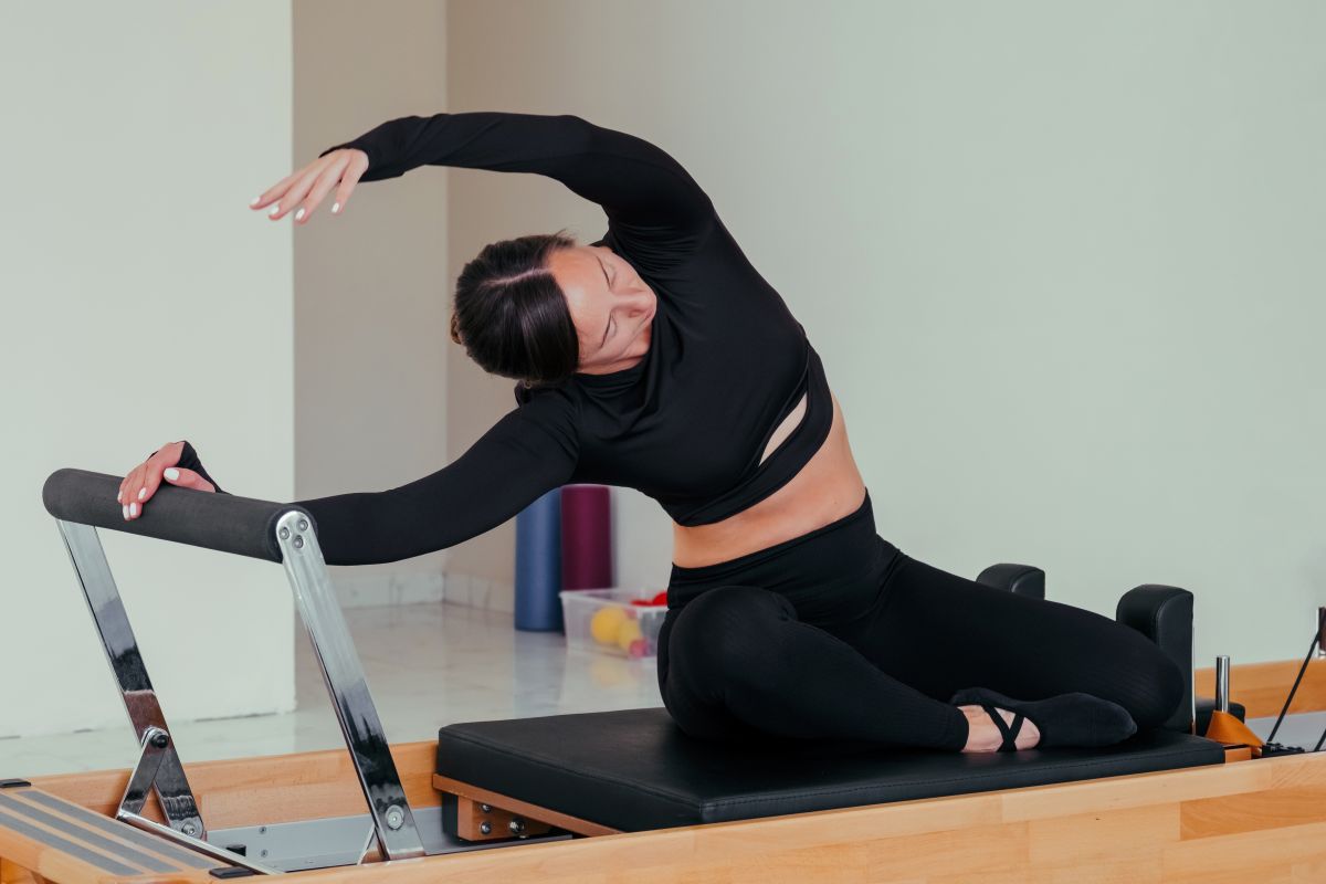 Woman performing a mermaid stretch on a Pilates reformer machine, demonstrating flexibility and core engagement in a studio setting