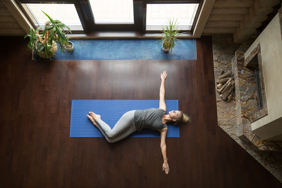 Woman performing a supine twist stretch on a Pilates mat, gently twisting her spine while lying on her back in a calm studio environment