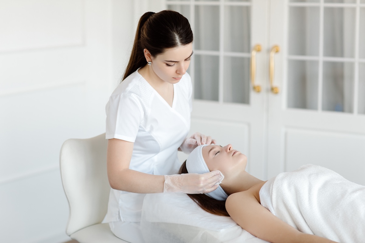 Beauty therapist cleansing a client’s skin before a cosmetic procedure, reflecting professional standards in the aesthetics industry.