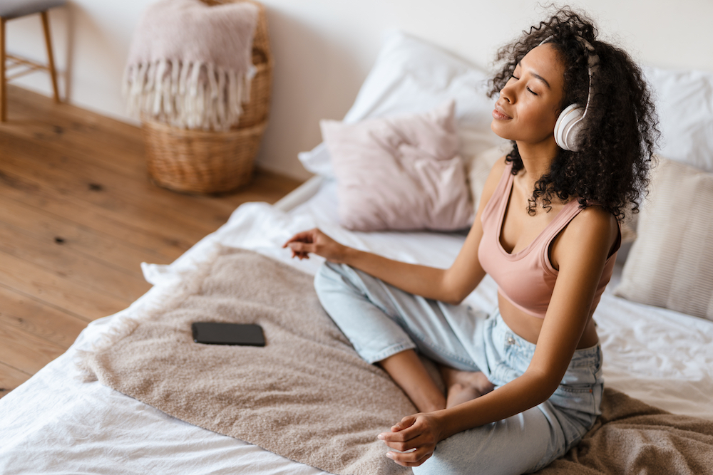 Woman sitting on her bed wearing headphones, meditating 