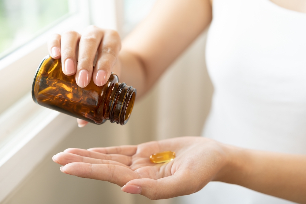 Person pouring vitamin supplement tablets into their hand from a dark glass jar