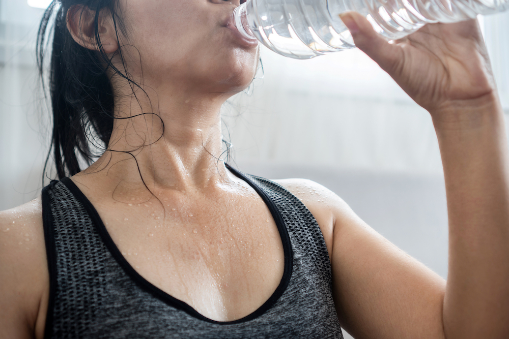 Woman in sports bra sweating, drinking water