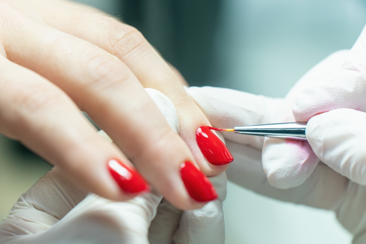 Nail technician applying red gel polish with a fine brush to avoid flooding the cuticle during a manicure