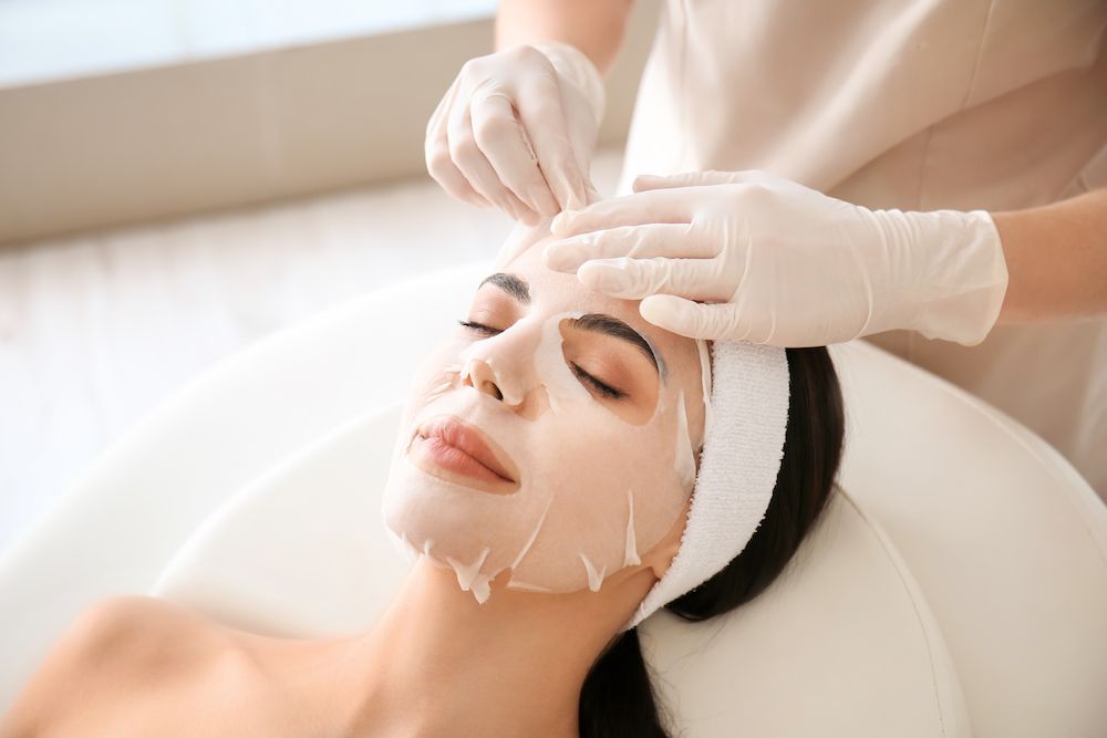 Therapist applying a sheet mask to a client in a salon 