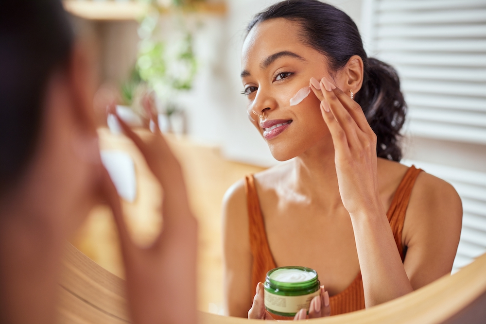 Woman applying a cream skincare product while looking in the mirror