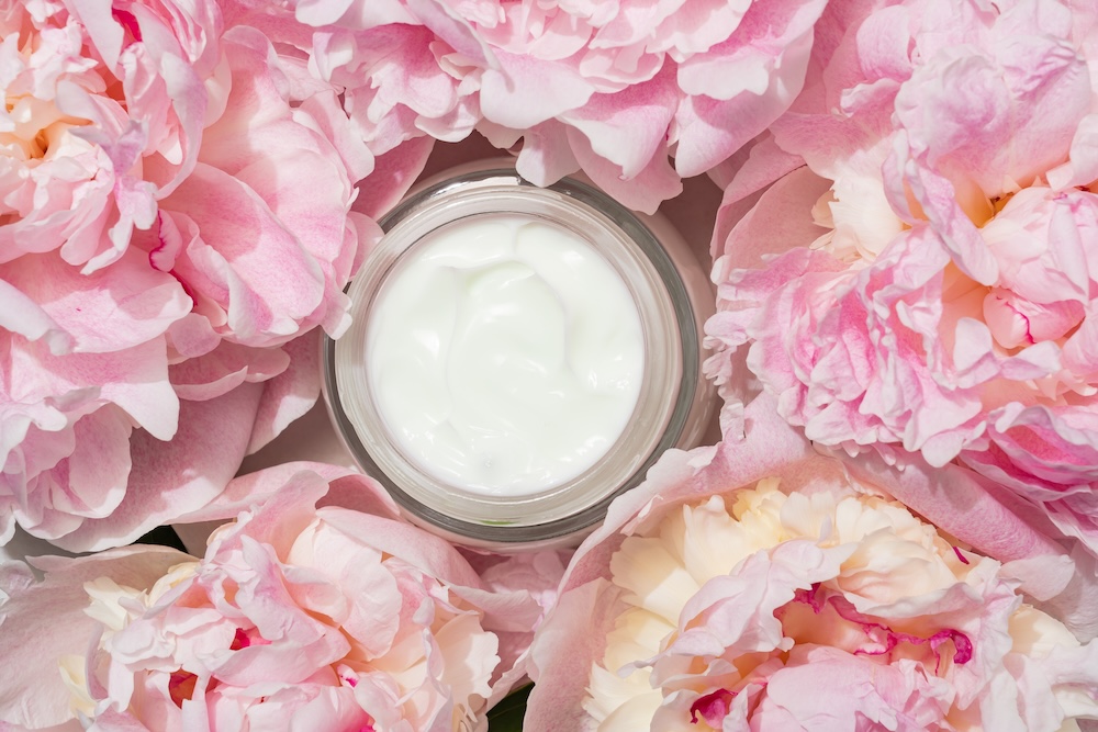 Pot of face cream surrounded by flowers representing sensory beauty experiences and mood-enhancing skincare trends