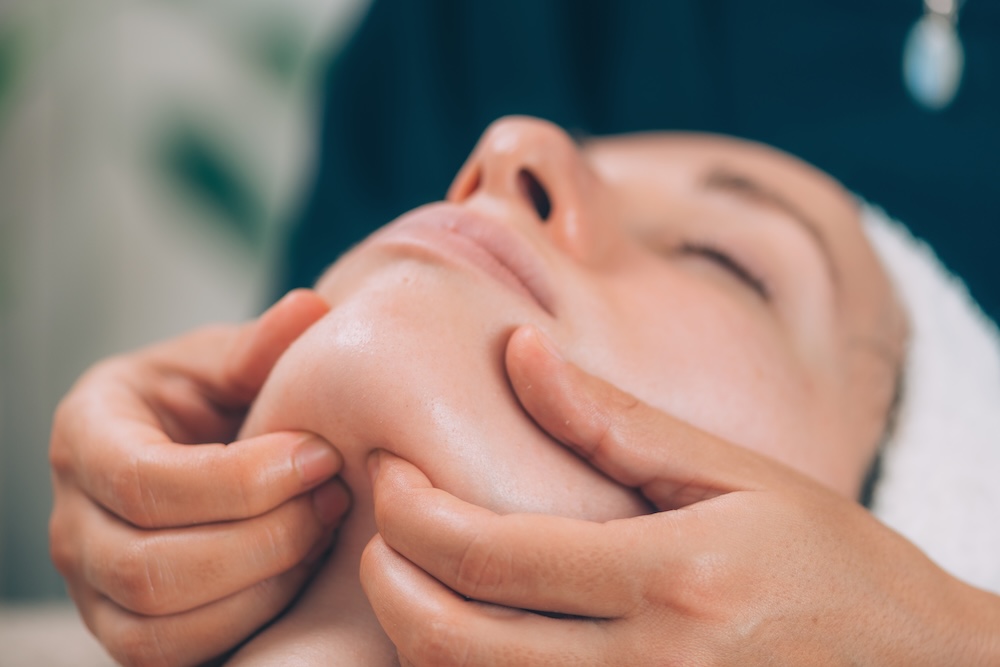 Woman receiving a jaw massage during a facial treatment to relieve tension and promote relaxation