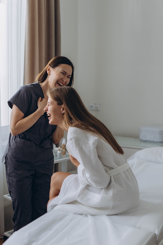Beauty therapist laughing and chatting with a client during a salon treatment, showcasing a positive and relaxed atmosphere