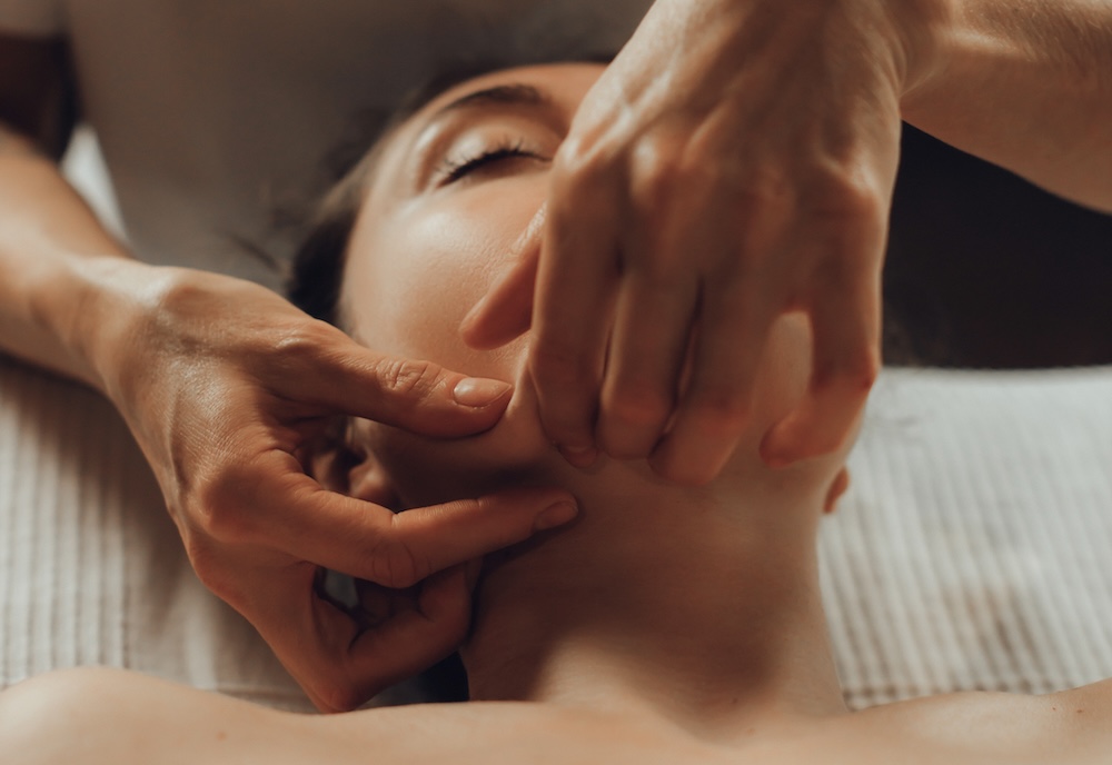 Beauty therapist performing a jawline facial massage to relieve muscle tension and sculpt the face