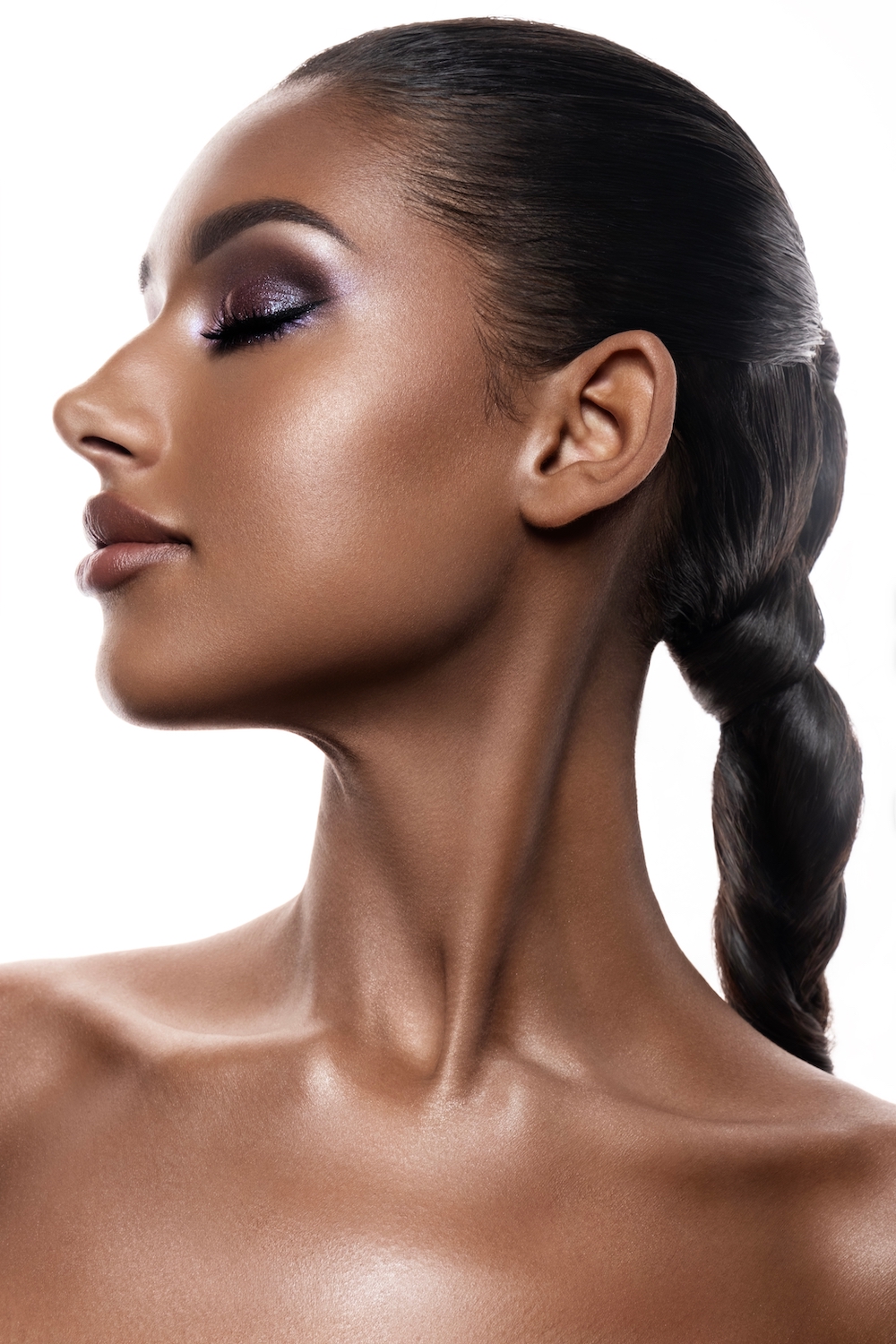 Side profile of woman with metallic purple eyeshadow and highlighter on cheekbones adding glow to skin