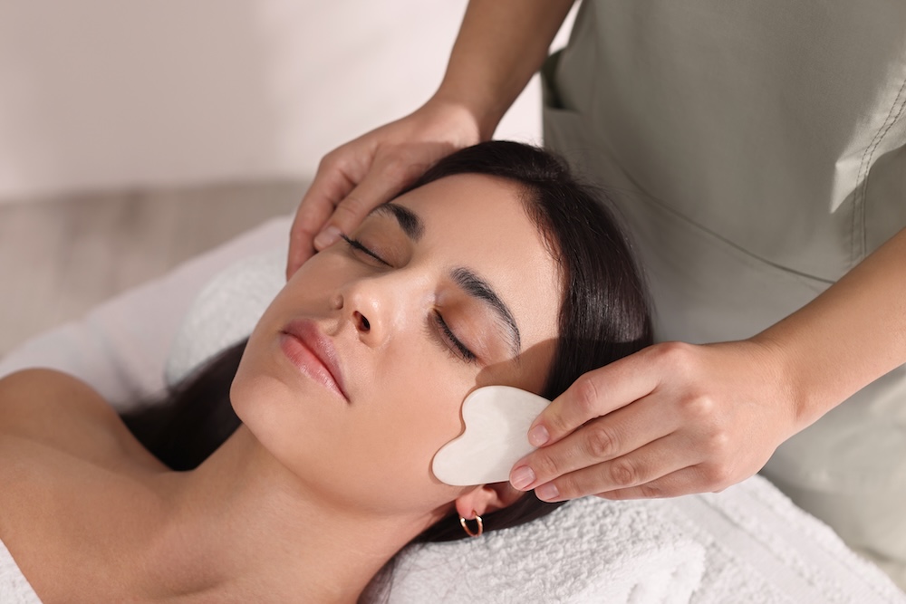 Beauty therapist performing a gua sha facial treatment using a crystal tool