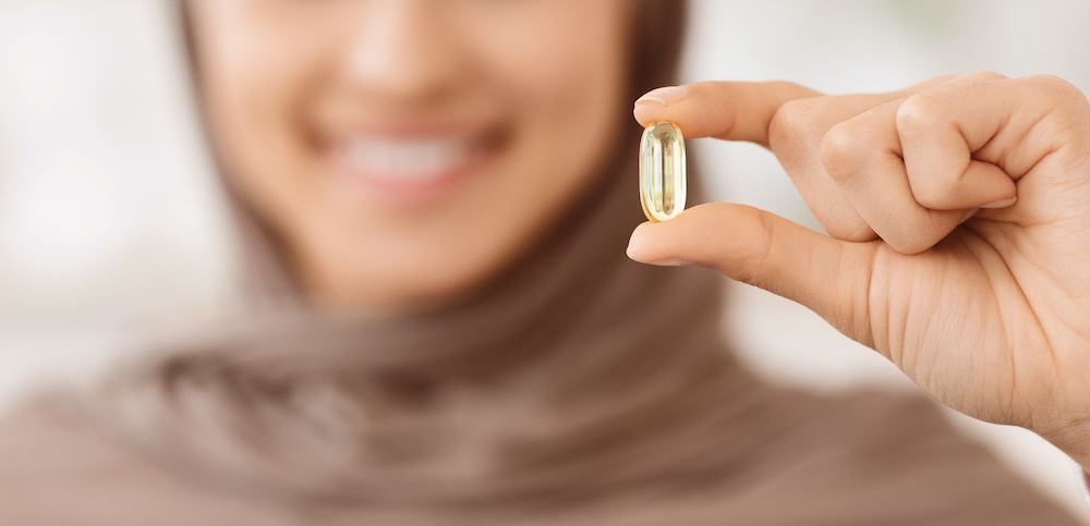 Woman hearing a hijab holding up a supplement capsule and smiling