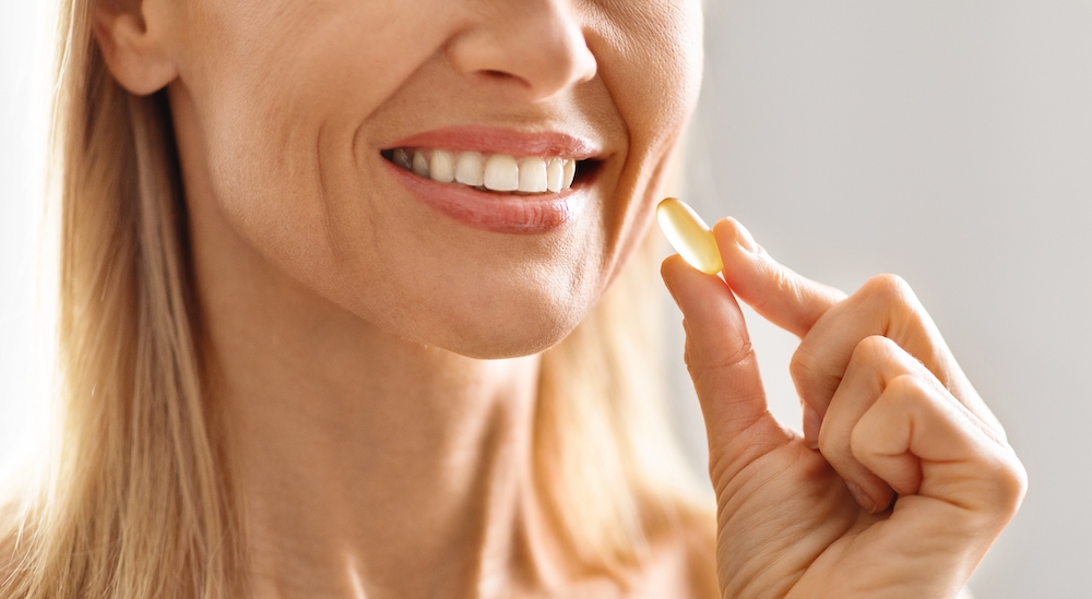 Woman smiling while holding a supplement capsule