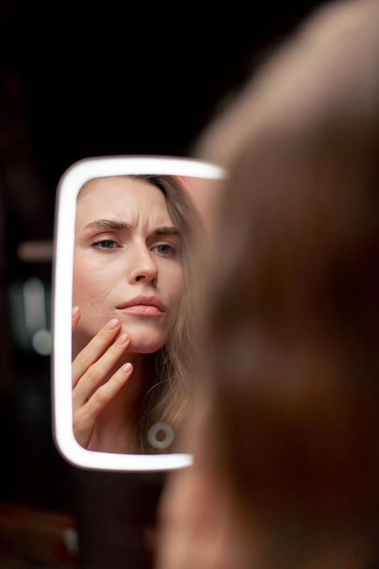 Woman looking at irritated, dry skin in a mirror, showing signs of an impaired skin barrier