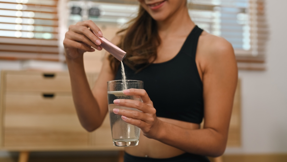 Woman in black sports bra pouring collagen sachet into water