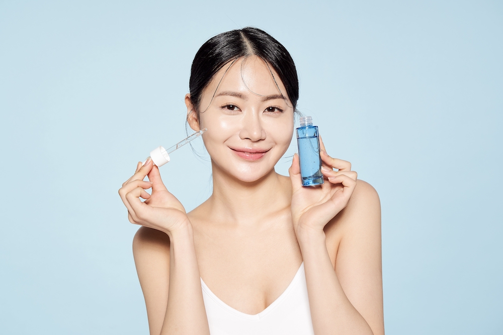 Korean woman holding up serum bottle and skincare pippette