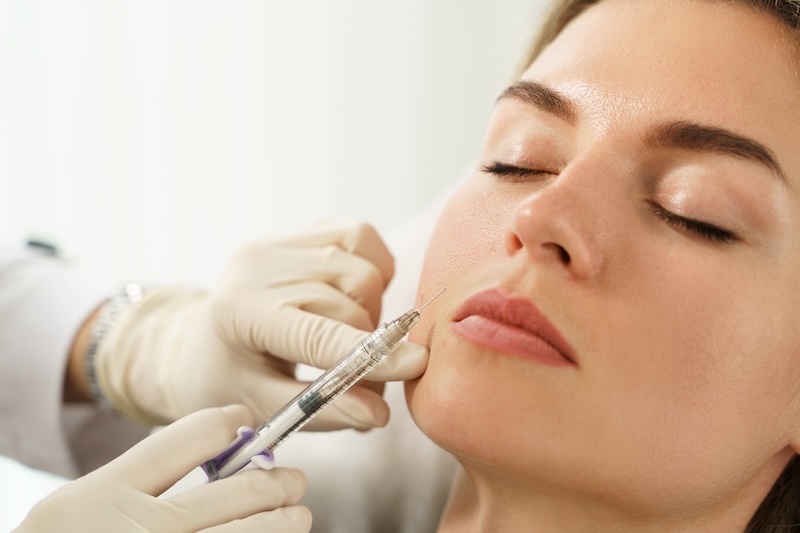 Practitioner administering dermal filler treatment to woman as a non-surgical cosmetic procedure in UK clinic
