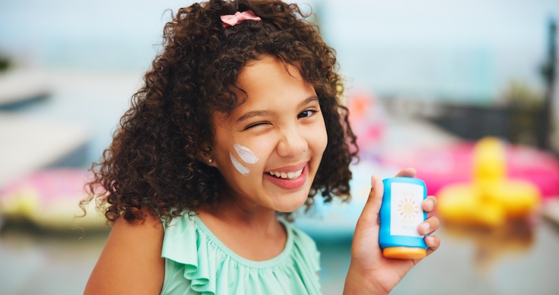 Pre-teen girl applying SPF sunscreen to her face outdoors