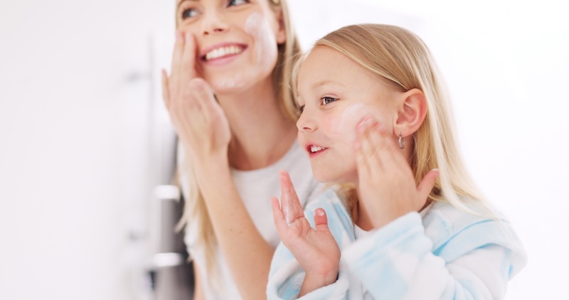 Young girl washing her face with her mother at the bathroom sink