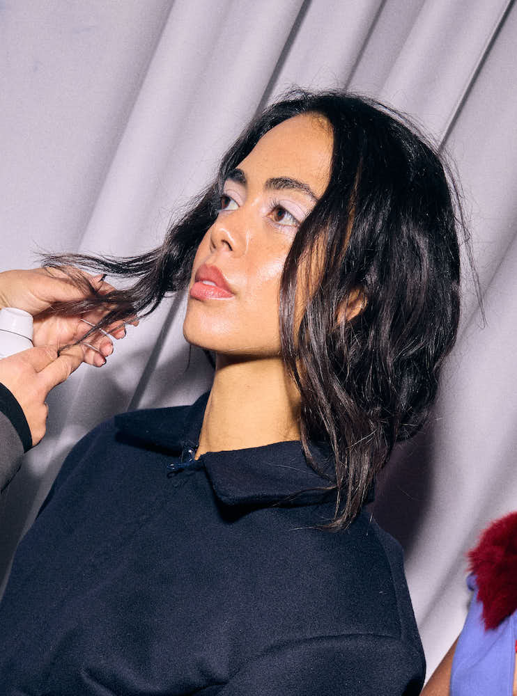 A model from Naomi Heart's LFW show having her hair fixed backstage; she has glowing skin and in wearing baby pink eyeshadow