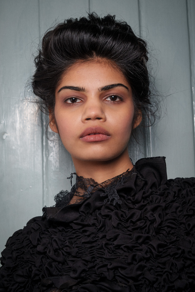 Model at the Dreaming Eli LFW show, with dark hair styled in a bouffant and smoky brown eye makeup and dark undereyes 