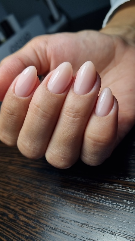 Hand showcasing classic nude sheer gel nails in an almond shape, perfect for a clean and wearable manicure look