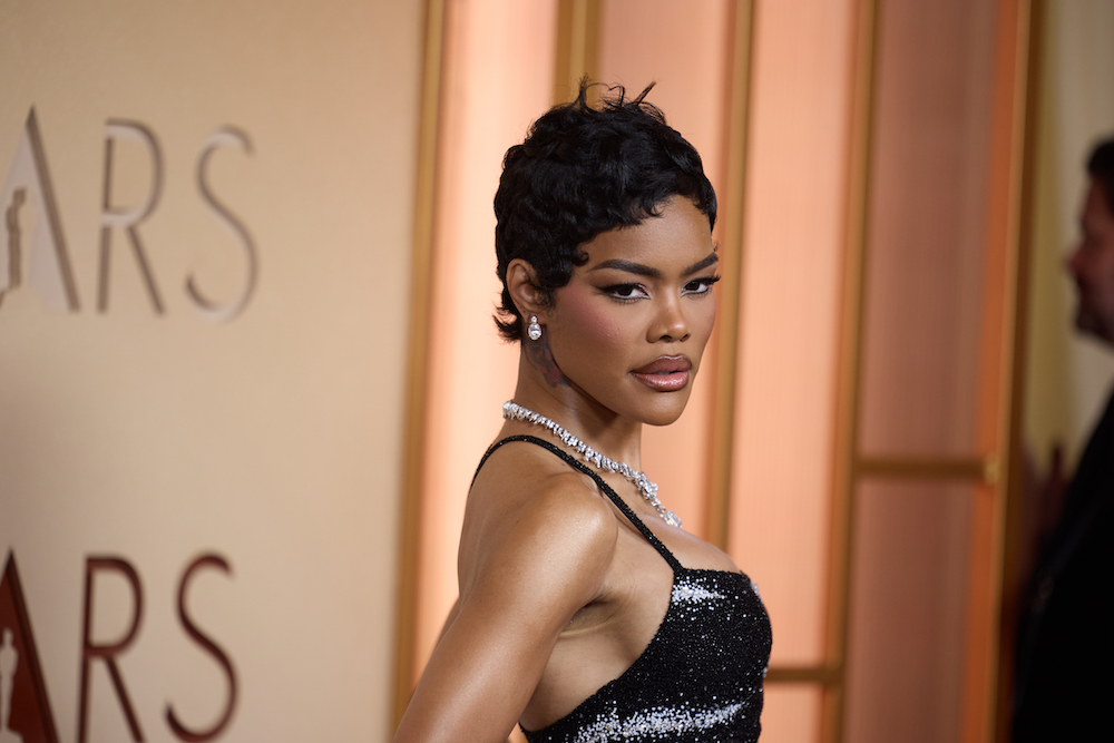 Actress Teyana Taylor poses on the Oscars red carpet wearing a black sequined gown and diamond jewelry, with a short pixie haircut and dramatic eyeliner makeup, against an Oscars backdrop.