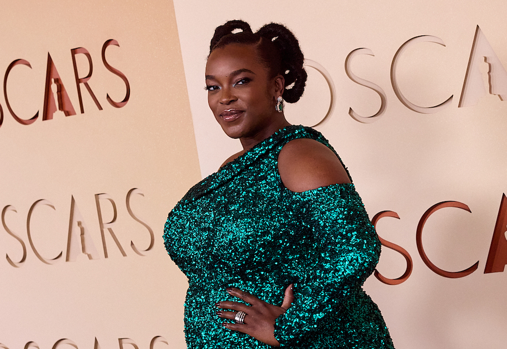 Actress Wunmi Mosaku poses on the Oscars red carpet wearing a shimmering emerald green sequined gown, with her hair styled in sculptural knots and green gemstone earrings.