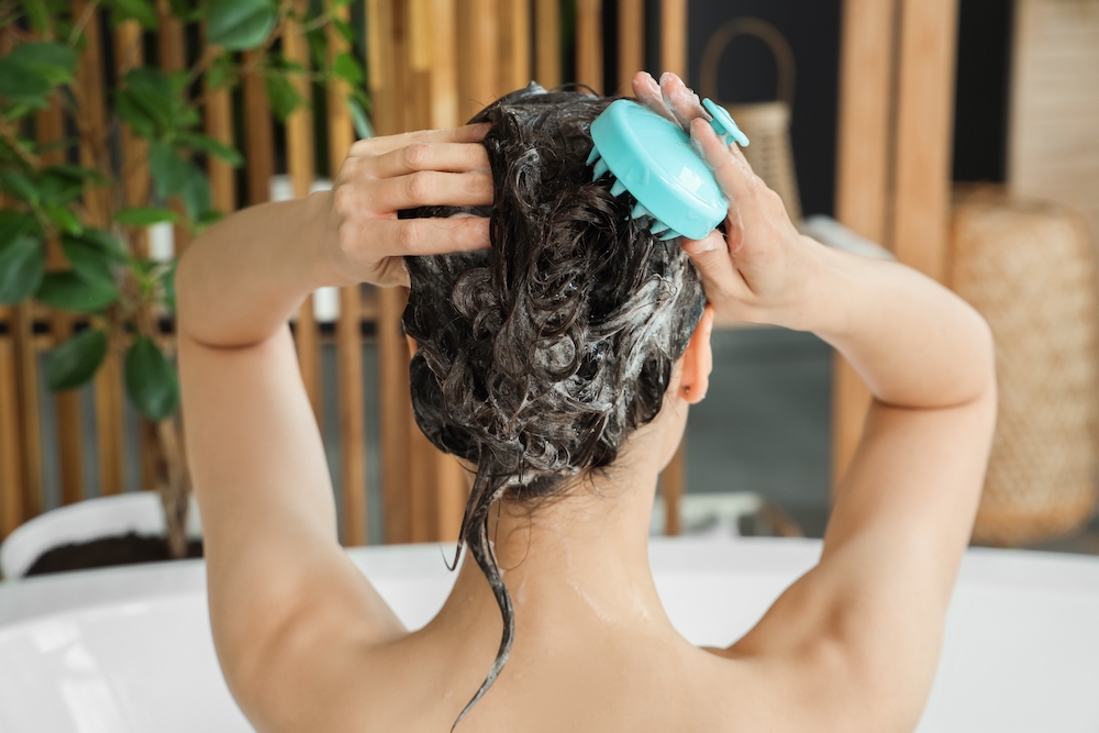 Woman using a scalp massage tool in the bath while washing her hair