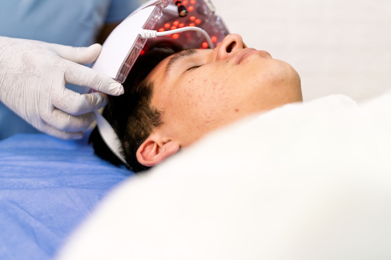 Man undergoing professional red light therapy with LED face mask to treat appearance of acne in clinic