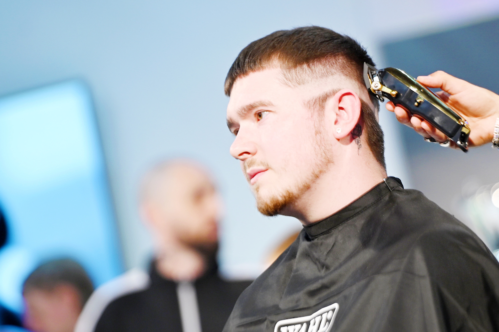 A male model sitting on stage having his hair cut by a Wahl ambassador, using a Wahl clipper