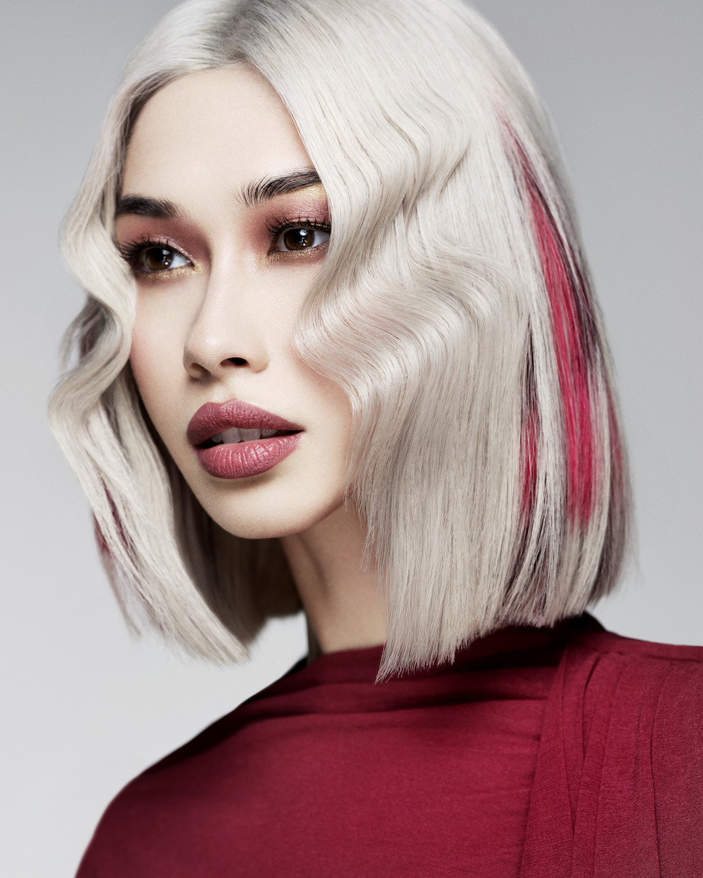 Model with a platinum blonde long bob (lob) with red and black colour panels, styled with a kink 