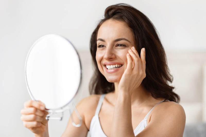 Woman looking in the mirror at glowing, hydrated skin results after nanoneedling treatment