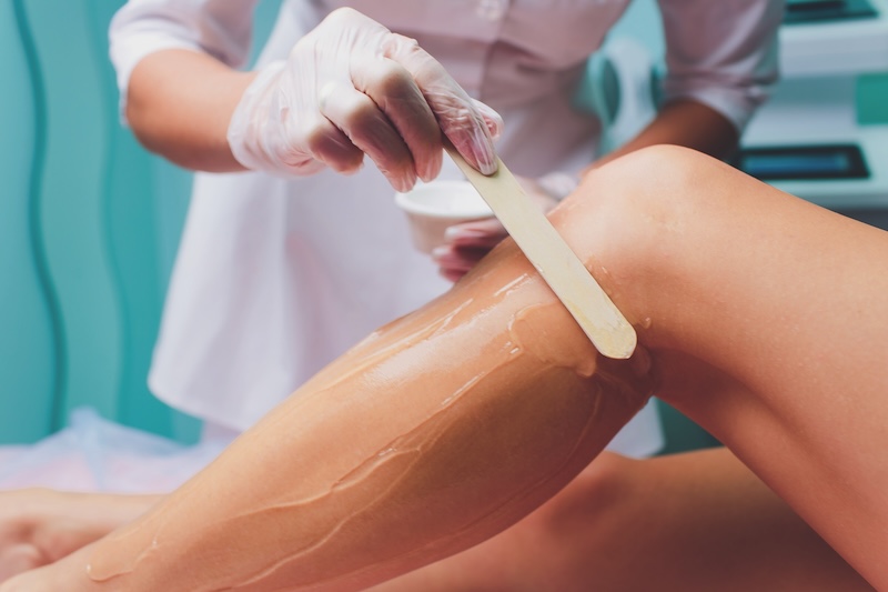 A waxing specialist applying warm wax to a client’s leg during a professional salon treatment focused on smooth skin results and careful technique