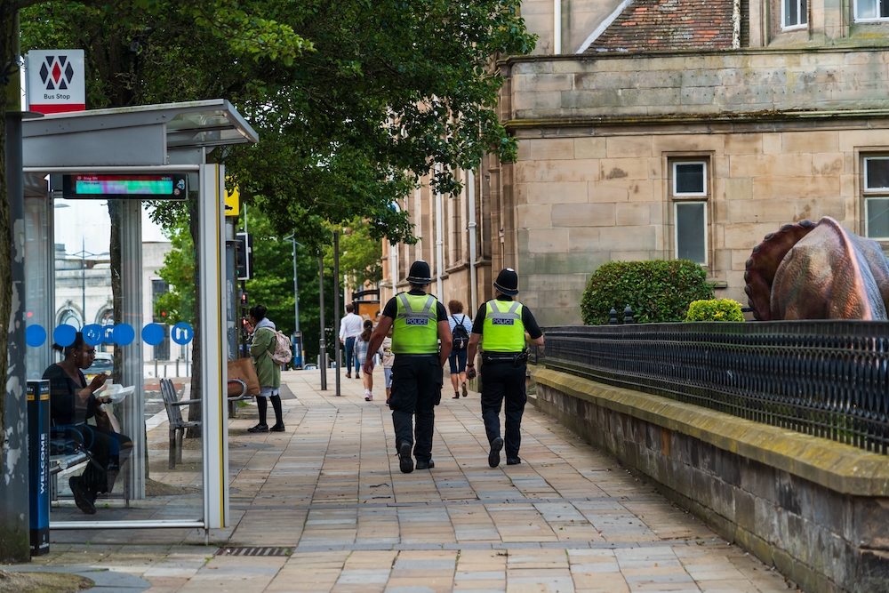 Two police officers in hi-vis uniform walking along a UK high street