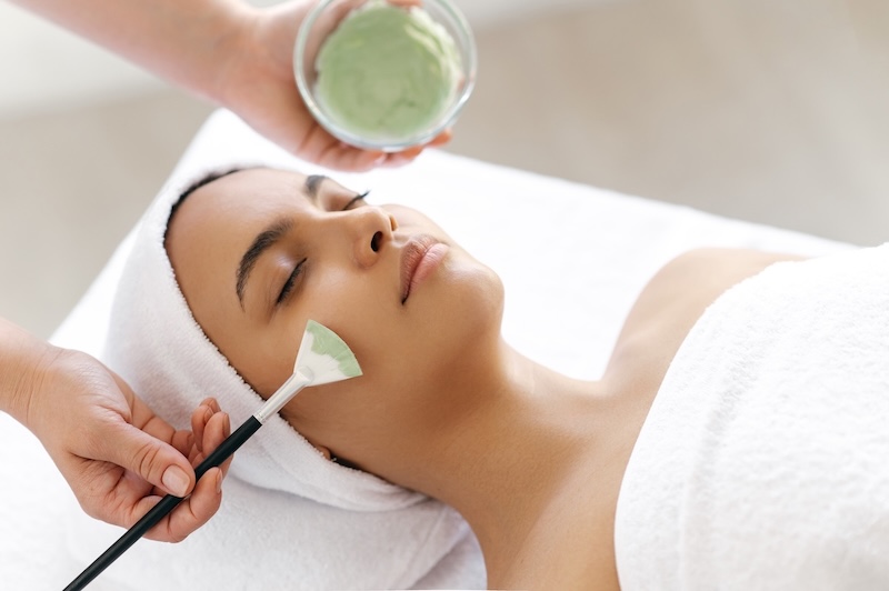 Facialist applying a green facial mask with a brush during a professional skincare treatment