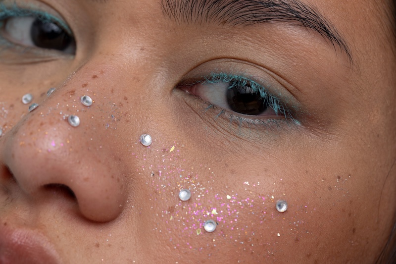 Close-up of festival-inspired smoky eye makeup with blue eyeliner, glitter and face gems from Pinterest’s Summer 2026 beauty trends