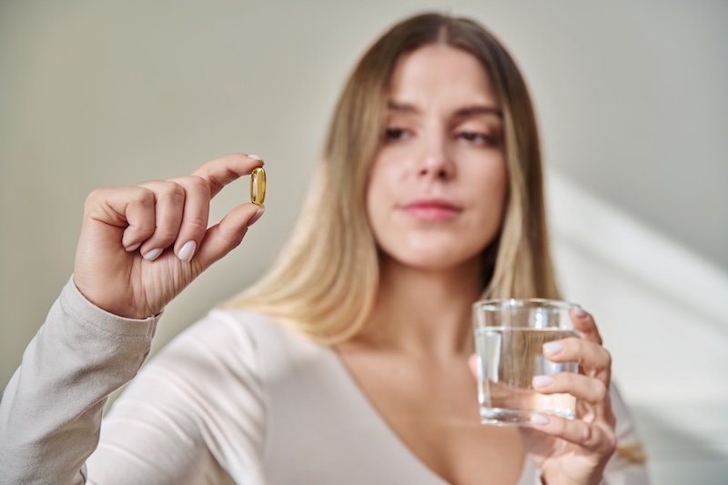 Woman looking at an omega-3 supplement pill as report highlights low oily fish intake