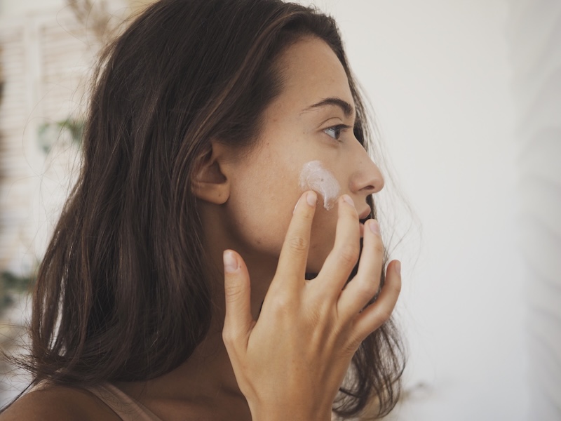 Young woman applying moisturiser to dry skin on her face