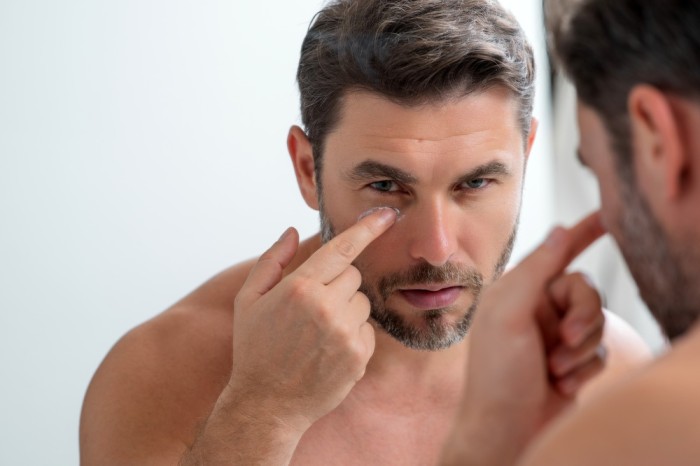 man posing in the mirror applying skin care cream to his face