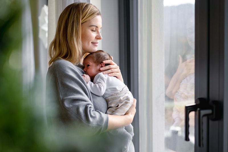 Postnatal client smiling while holding her baby, reflecting maternal wellbeing and support after birth