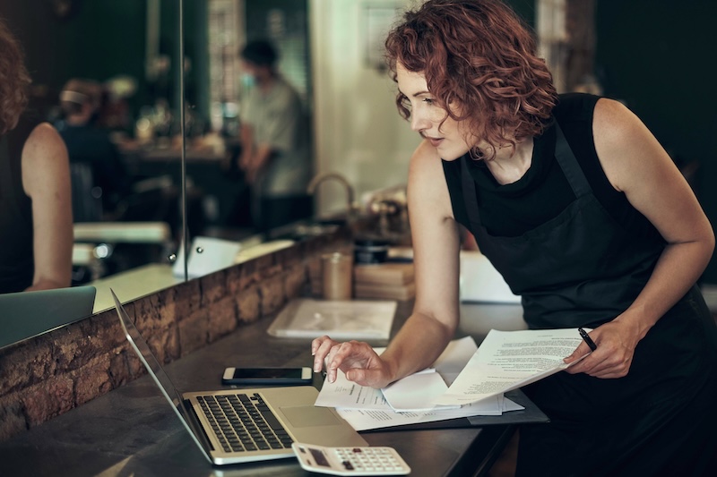 Beauty professional reviewing clinic documentation and compliance paperwork on a laptop before performing advanced skin treatments