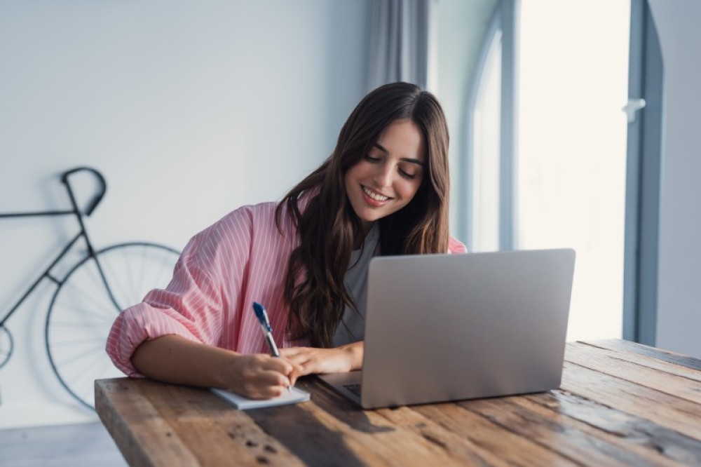 lady writing notes on a desk in front of laptop