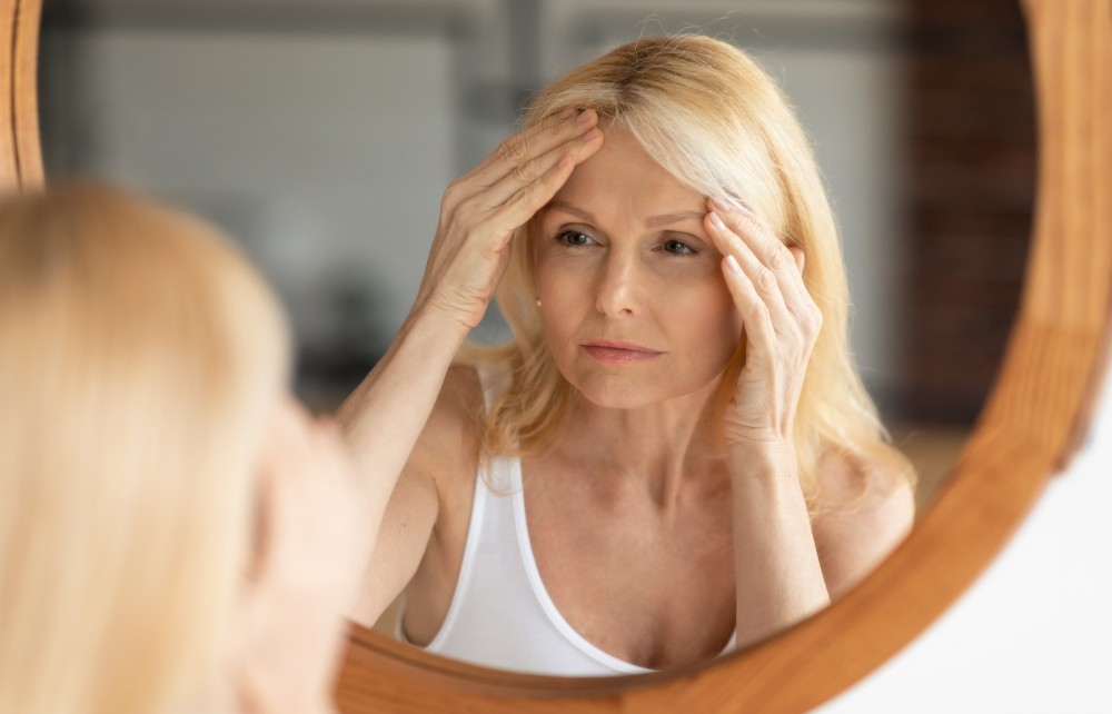 older blonde lady looking at skin in the mirror