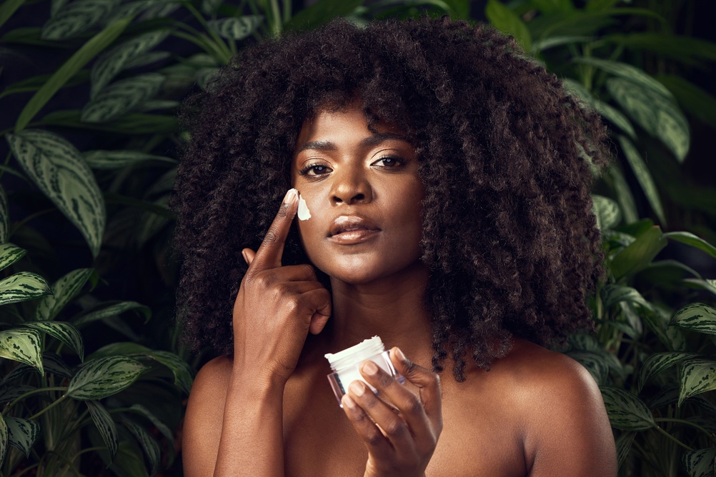 lady applying skincare cream in front of green nature backdrop