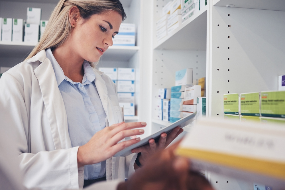seo alt text  Pharmacist reviewing medication stock on a tablet in a pharmacy.