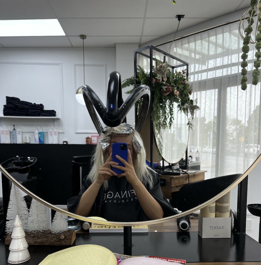 Influencer taking a mirror selfie while getting her hair done in salon
