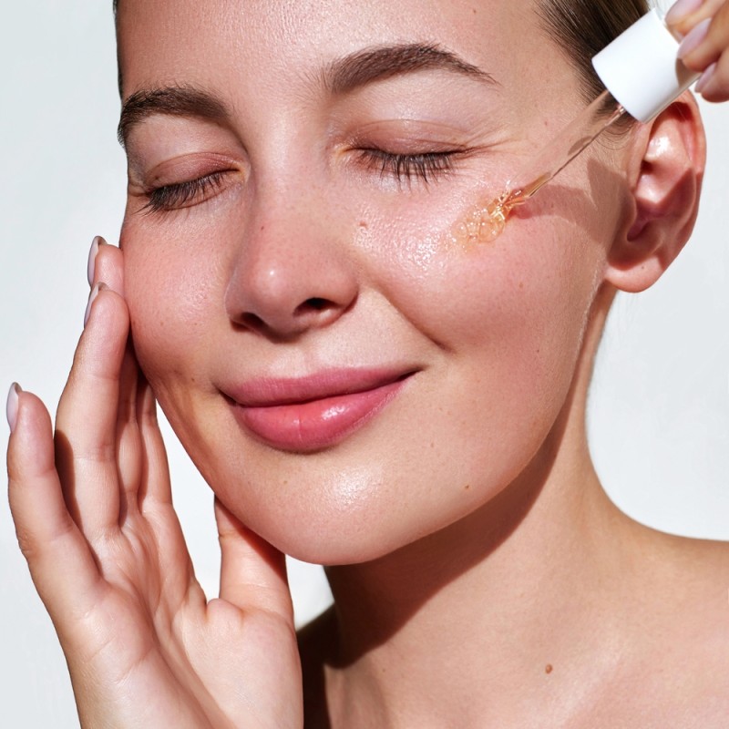 Woman applying a topical serum to her cheek using a dropper