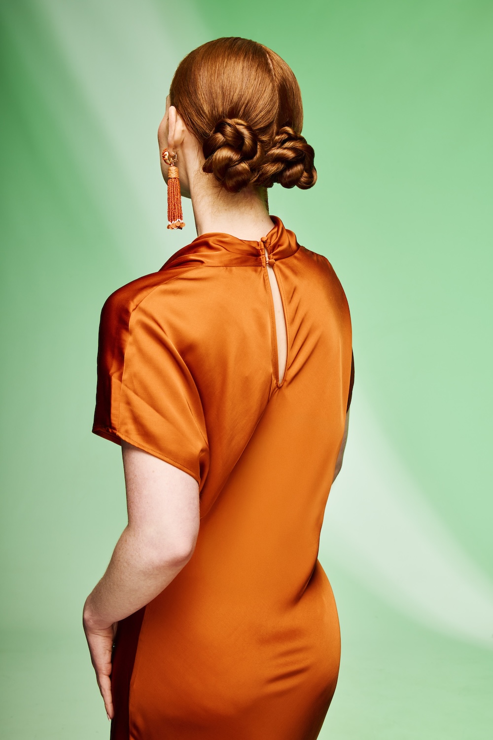 Model with copper hair styled in two twisted low buns, with a sleek centre parting